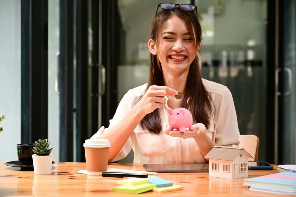 Cheerful young woman putting coin into piggy bank. Saving money or savings concept.
