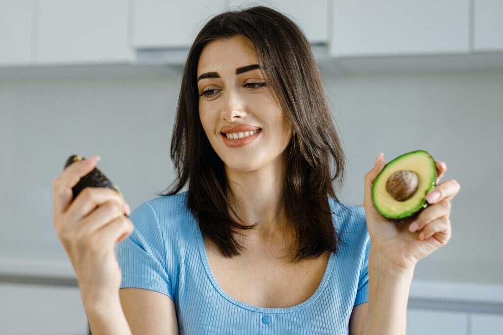 Female nutritionist show avocado fresh vegetables and a tape measure on her table