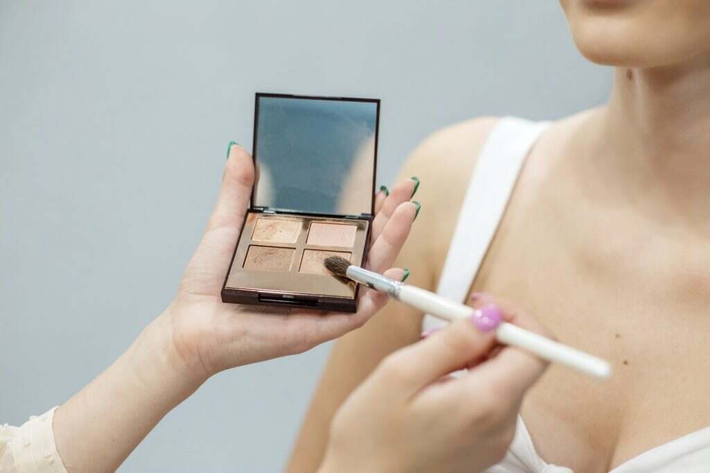 Makeup artist blonde prepares cosmetics for make-up. Pale brown eyeshadow palette.