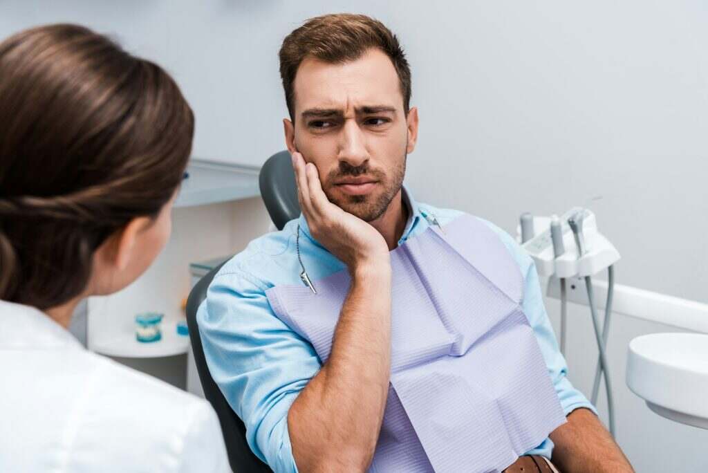 selective focus of upset patient touching face while having toothache near dentist