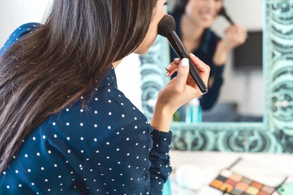 Young woman applying makeup while looking in mirror