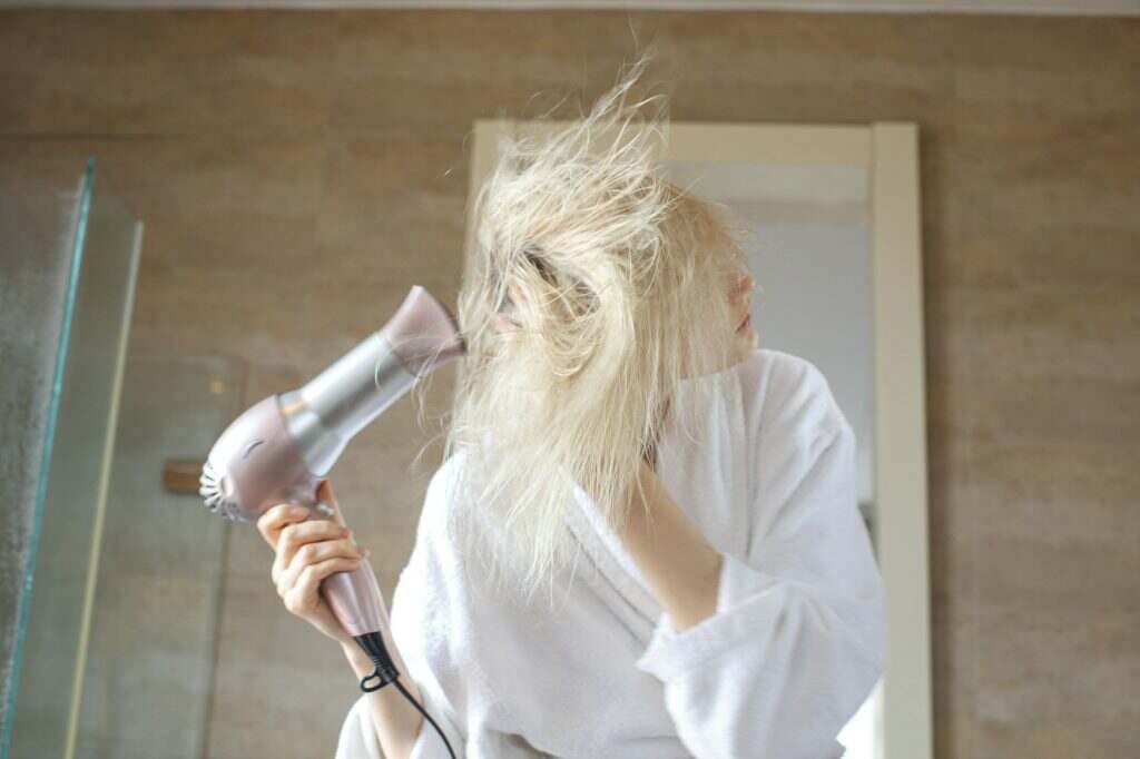 blonde woman drying hair with hair dryer