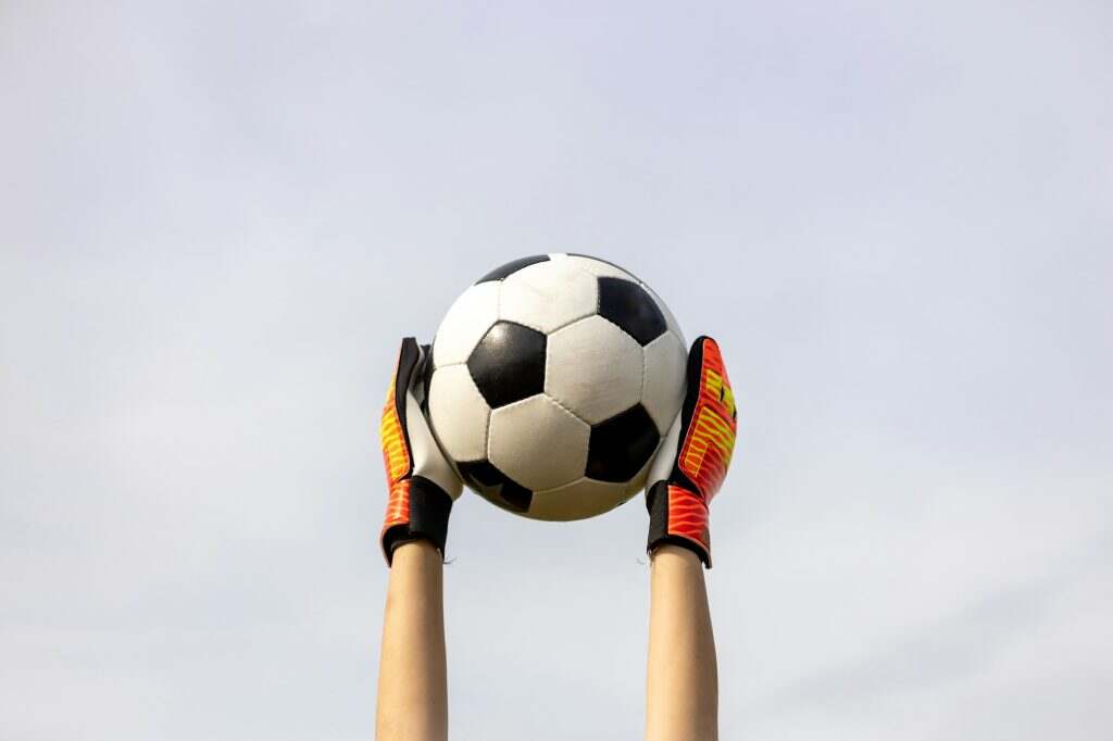 Hands with goalkeeper's gloves holding the soccer ball in the air