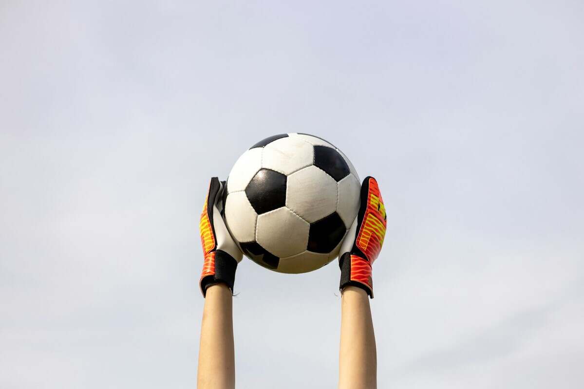 Hands with goalkeeper's gloves holding the soccer ball in the air