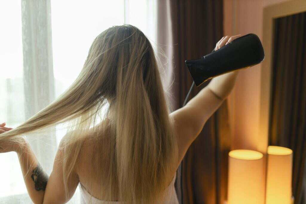 Happy woman drying her hair in bathroom. Hair care. Beautiful smiling woman drying healthy hair