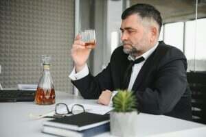 Old business man is drinking alchool at the office