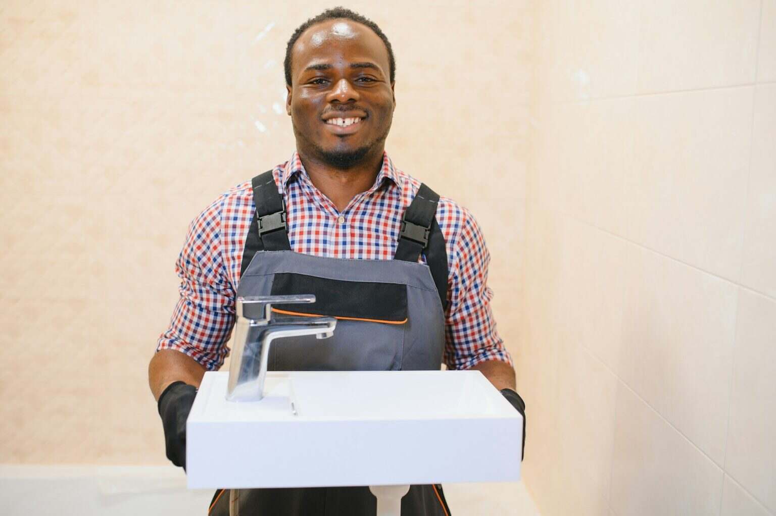 Side View Of Young African Male Plumber Fixing Sink In Bathroom