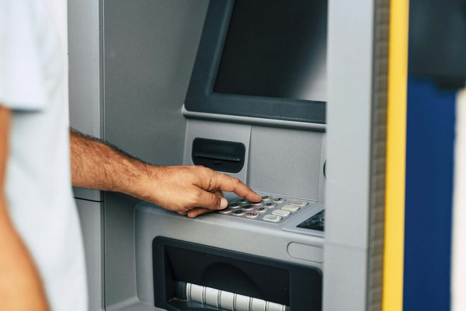 Close up of man hand withdrawing money at automatic atm machine typing secret security code