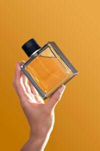 Perfume bottle in hands on an orange background.