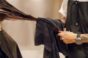 Close up of hairdresser is wrapping the wet hair of woman in towel after washing