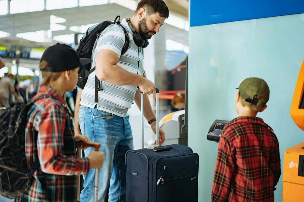 caucasian bearded man with children in airport putting suitcase on weights mesuring luggage