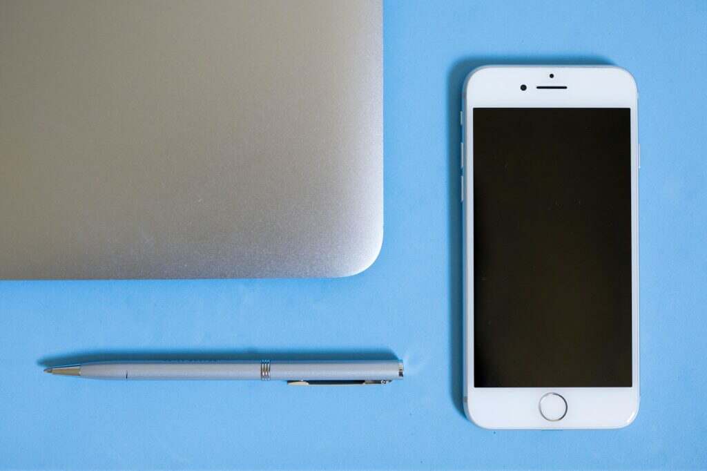 Flatlay view looking down at a silver computer laptop apple phone pen on a blank blue background bac