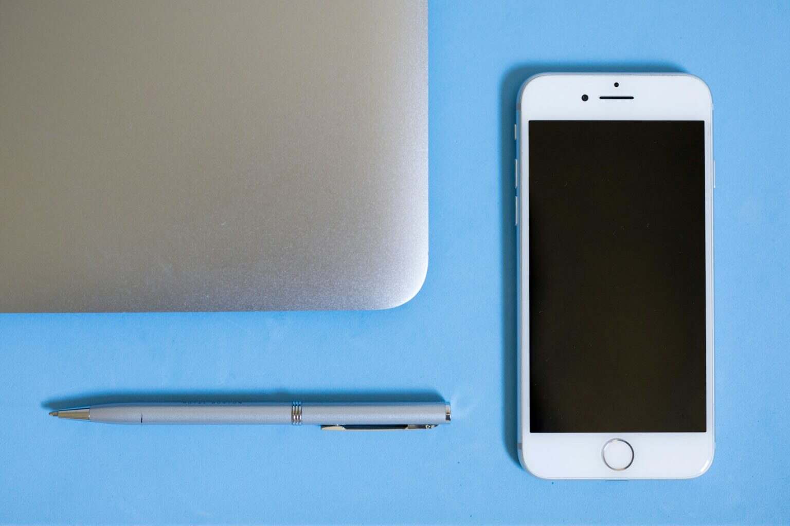 Flatlay view looking down at a silver computer laptop apple phone pen on a blank blue background bac