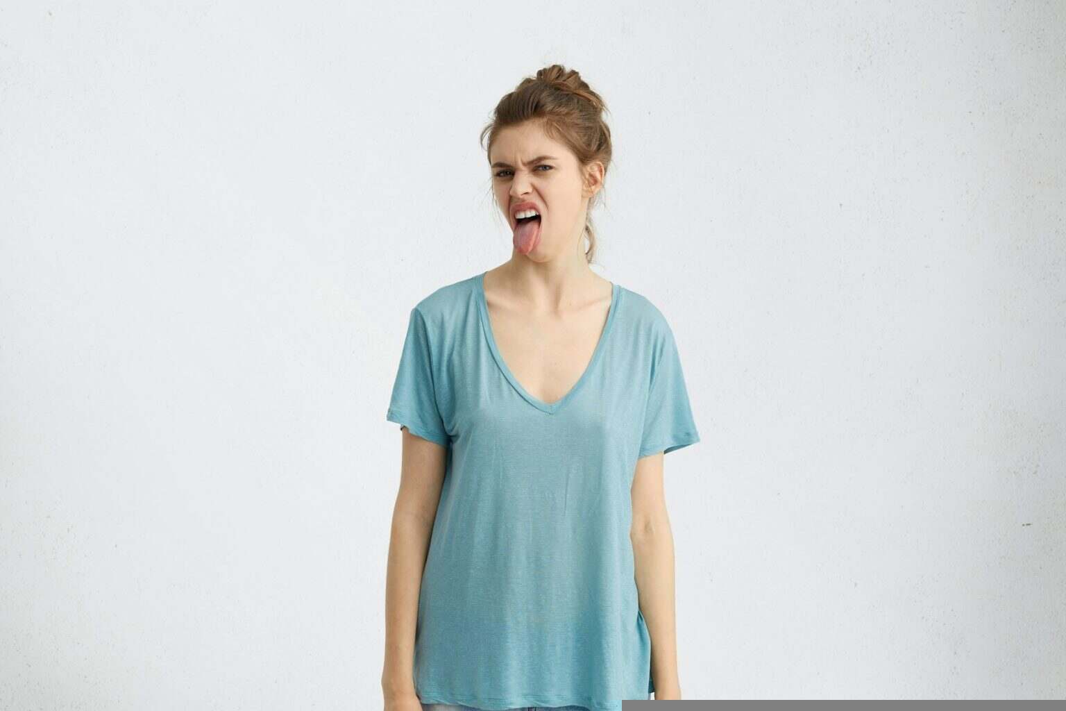 Irritated young woman with grumpy expression, showing tongue while being dissatisfied with something