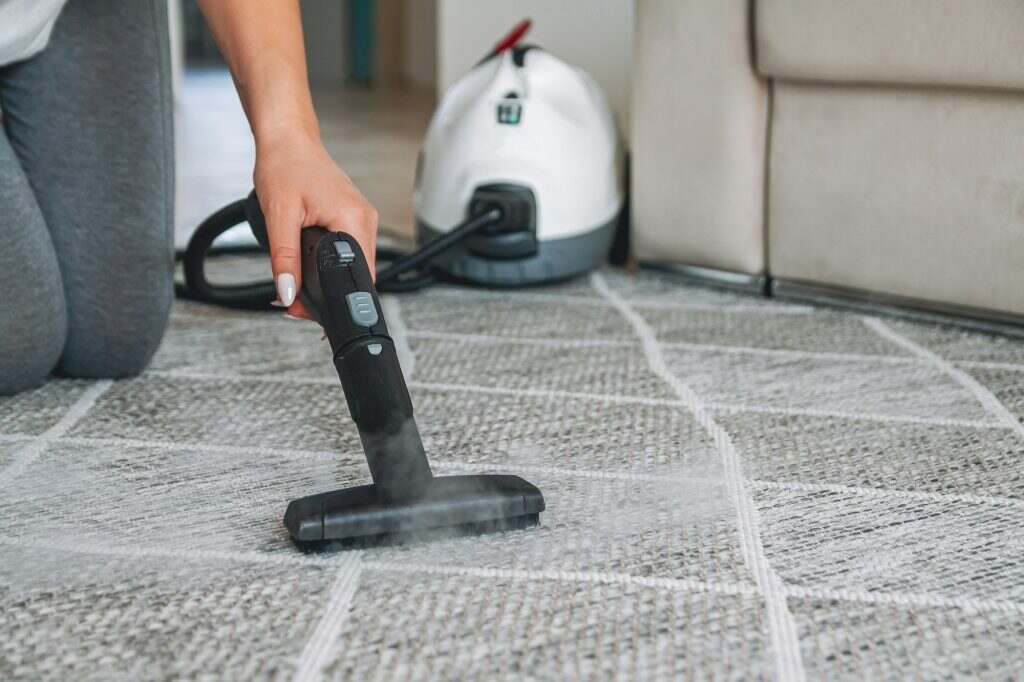 Comment nettoyer un tapis efficacement ? Woman cleaning carpet with a steam cleaner