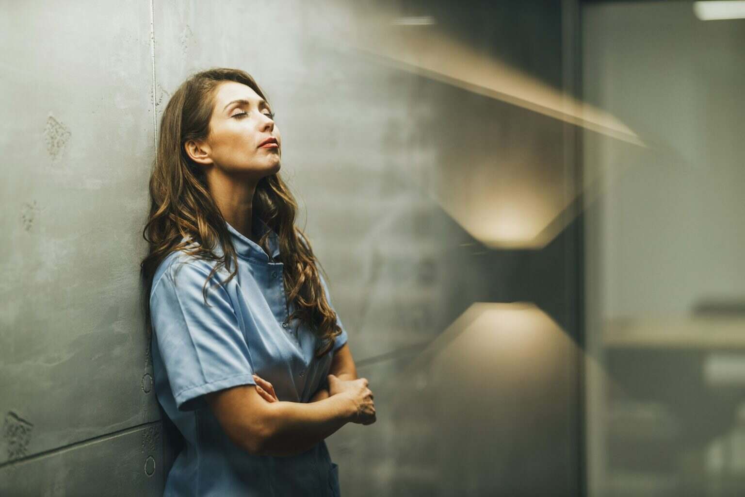 Nurse With Arms Crossed Having Quick Break In Empty Hospital Hallway
