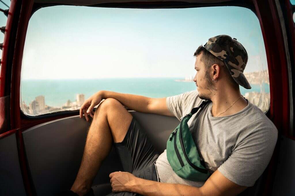 L’Accessoire indispensable : le sac Banane, entre praticité et style Young man is enjoying the seascape from the cable car wearing a camouflage cap and a fanny pack