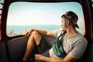 Young man is enjoying the seascape from the cable car wearing a camouflage cap and a fanny pack