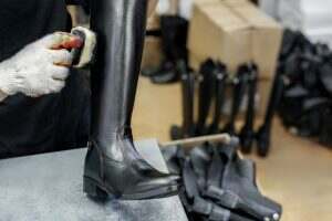 A shoemaker cleans leather boots in the workshop.