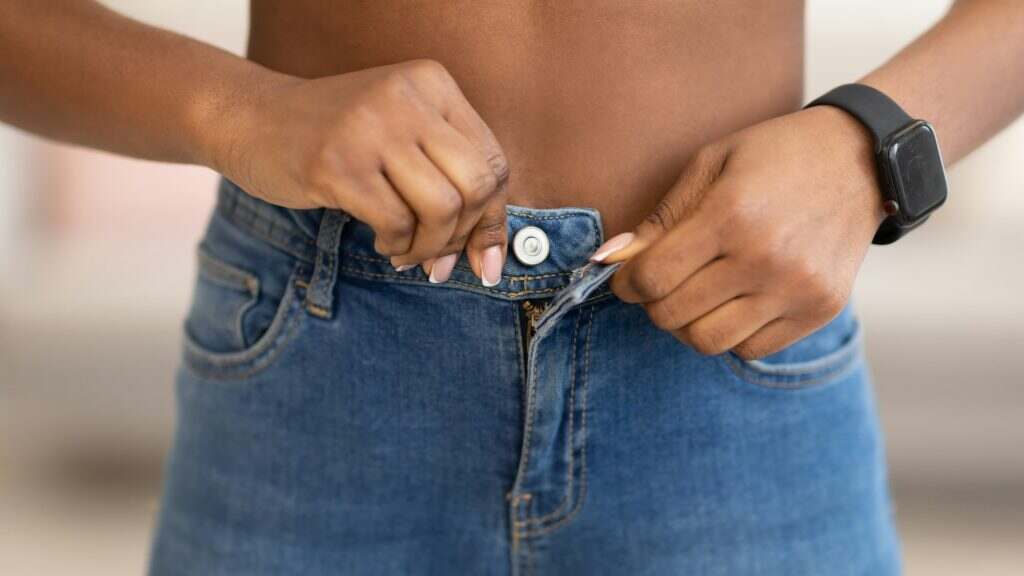 African Female Buttoning Skinny Jeans After Weight Loss Indoors, Closeup