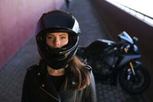 Attractive serious woman is standing next to her motobike