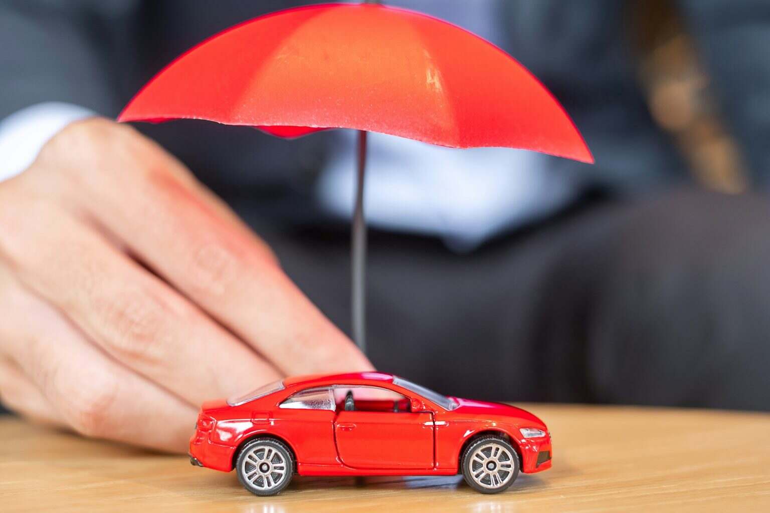 Businessman hand holding umbrella cover or protection red car toy on table. Car insurance concept