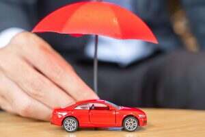 Businessman hand holding umbrella cover or protection red car toy on table. Car insurance concept