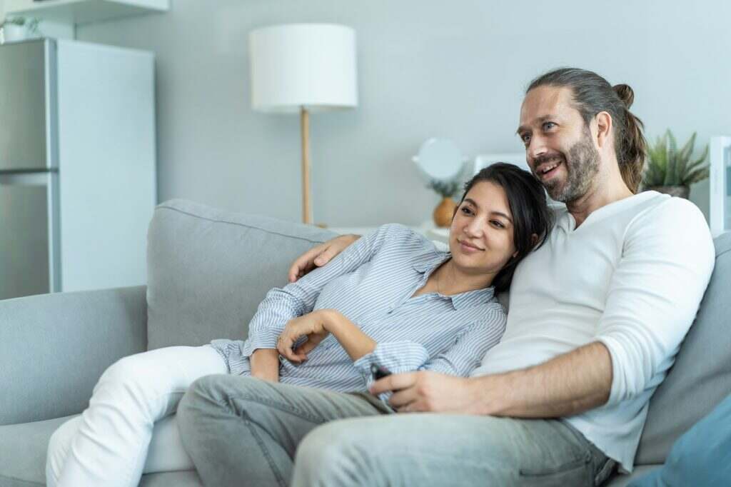 Caucasian loving couple watch movie on television together in living room at home.