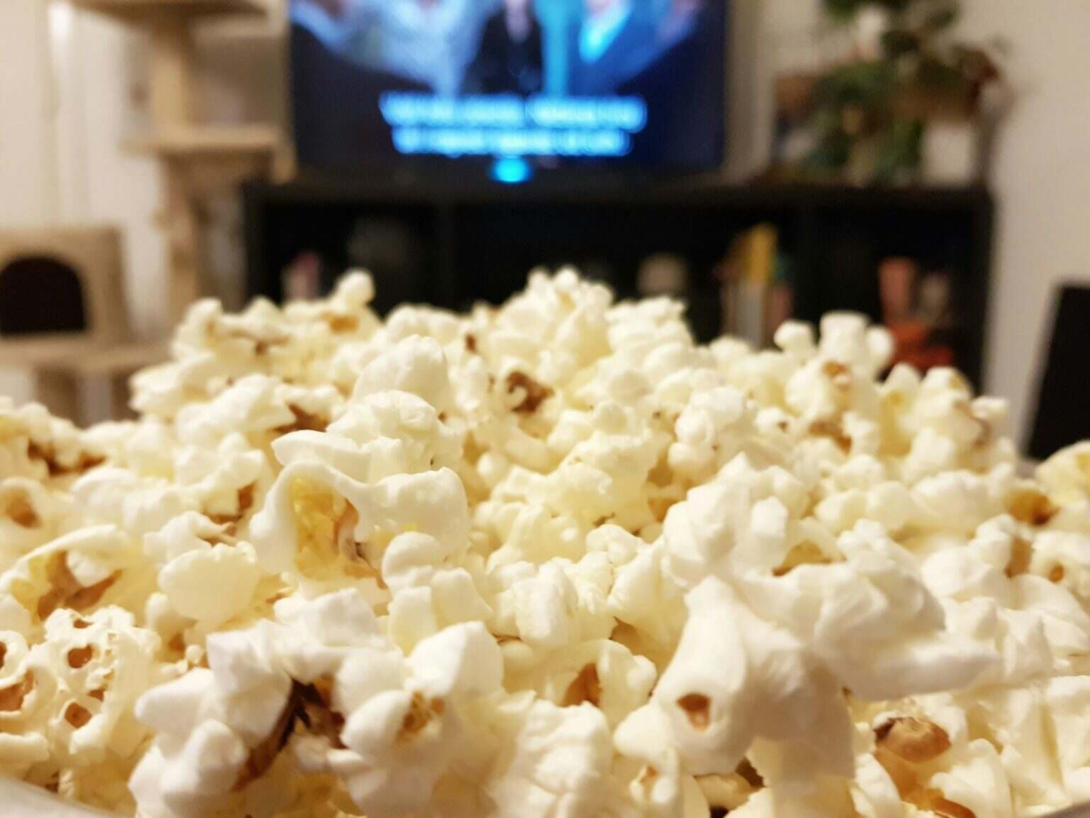 Close-up selective focus image of popcorn in front of tv.