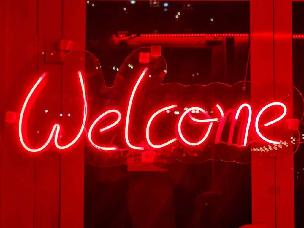 Closeup of red welcome neon sign hanging on the window of bar or night club
