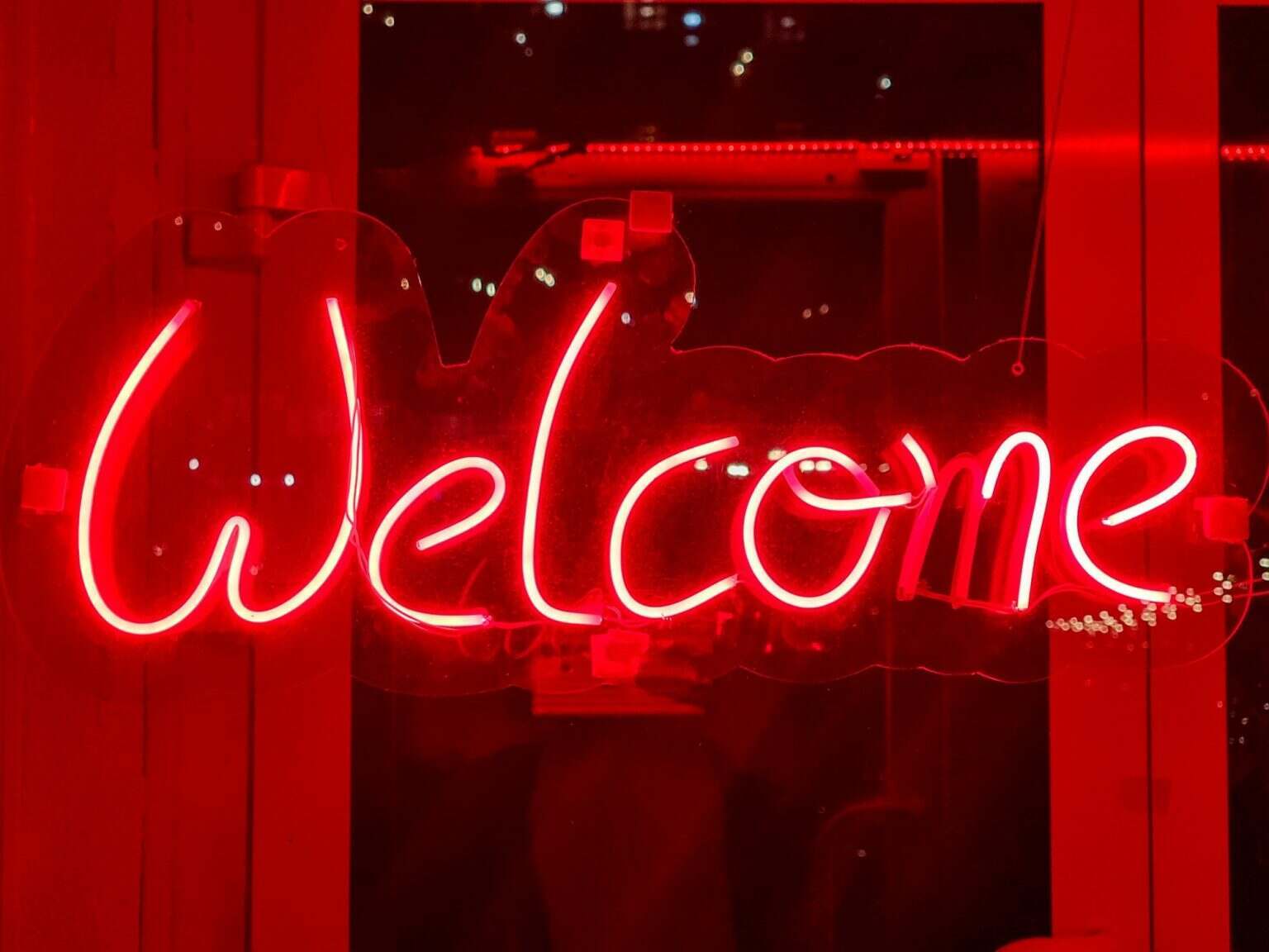 Closeup of red welcome neon sign hanging on the window of bar or night club