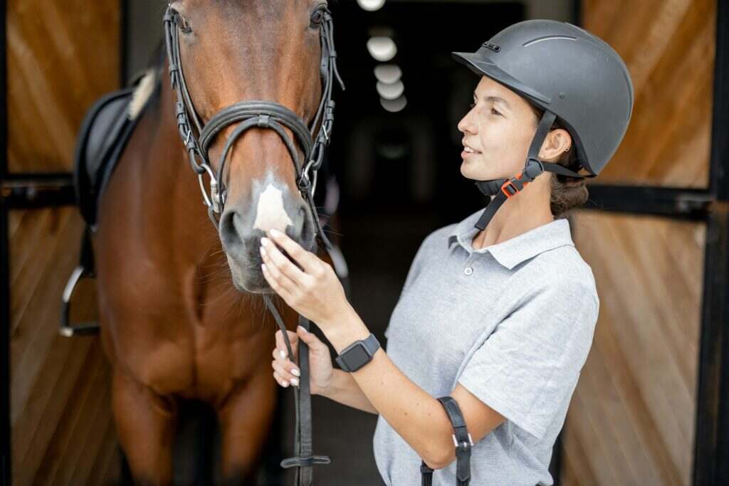 Female horseman with Thoroughbred horse in stable