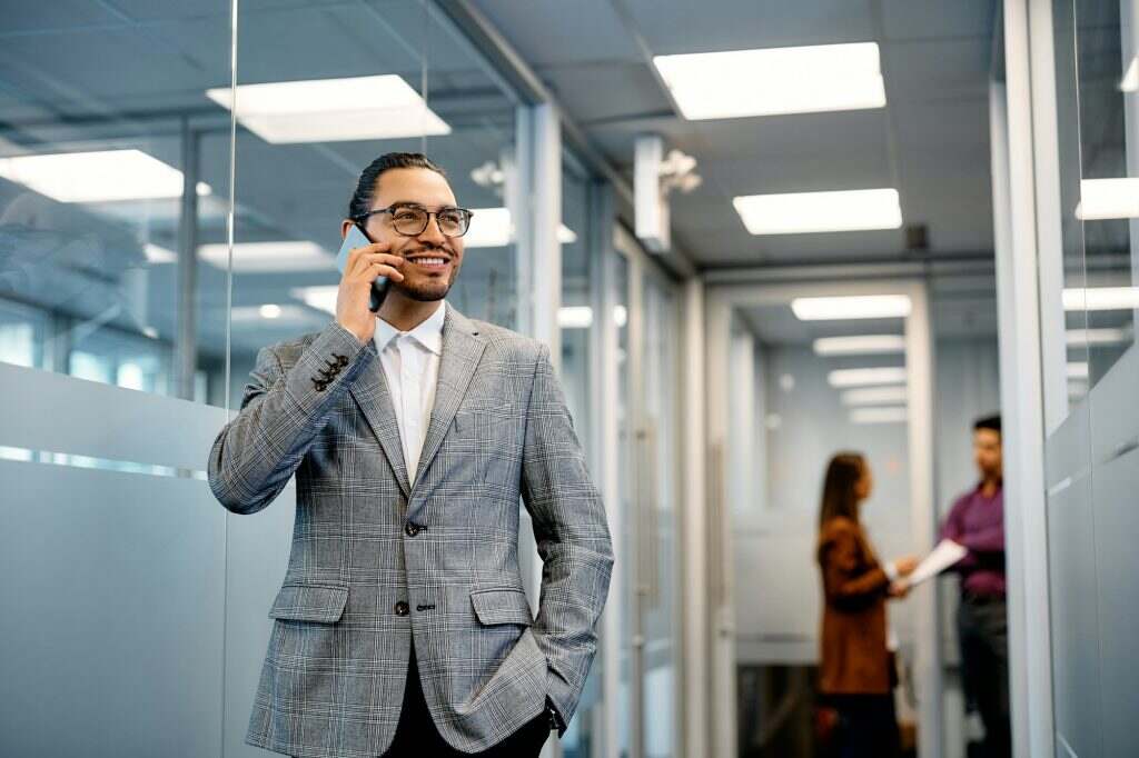 Happy Hispanic businessman talking on the phone in hallway.
