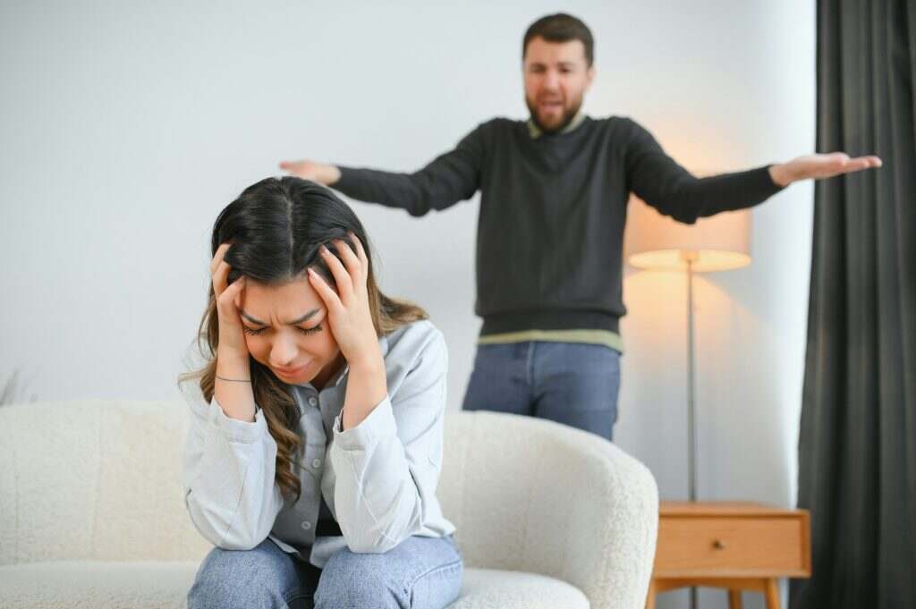 Irritated husband is shouting at his wife with violence. Woman is covering her face with fear
