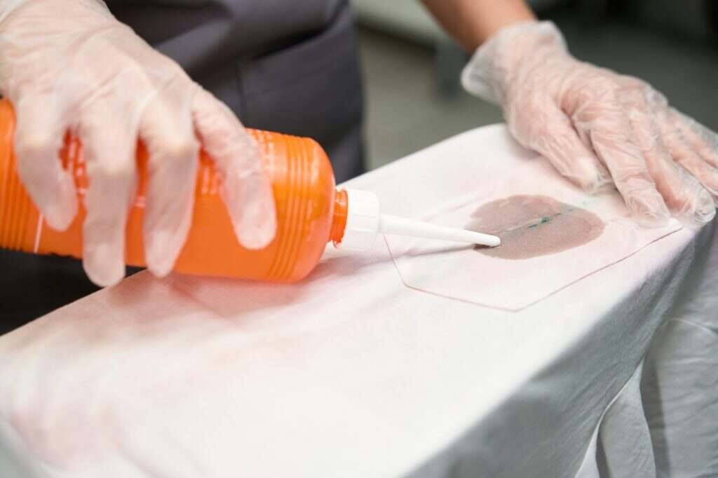 Comment éliminer efficacement les taches de fruits sur vos textiles ? Laundry worker treating dirty spots on clothes before dry cleaning