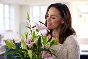 Smiling Woman At Home Smelling And Arranging Bouquet Of Flowers In Glass Vase