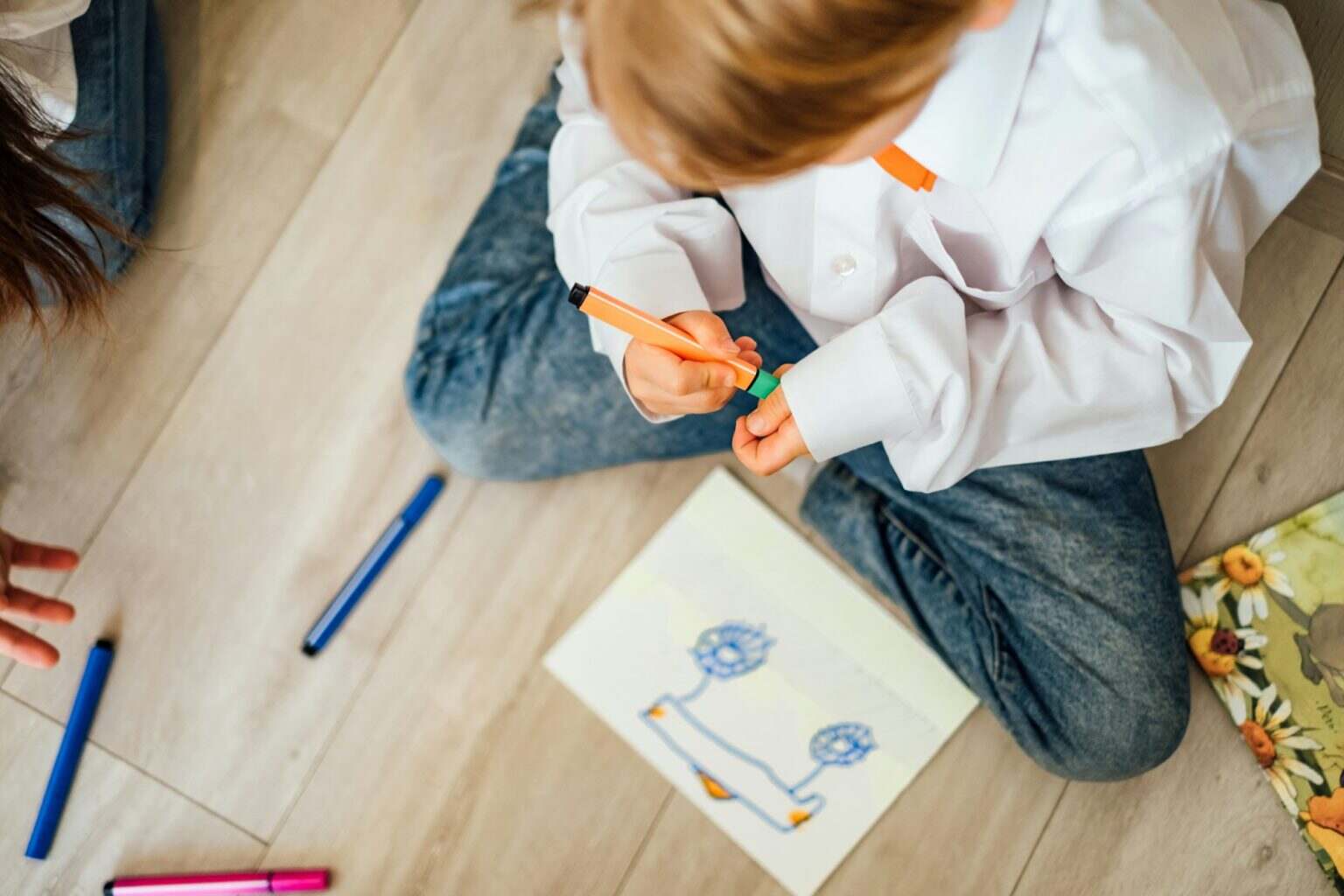 The boy draws a car with felt-tip pens, sitting on the floor at home