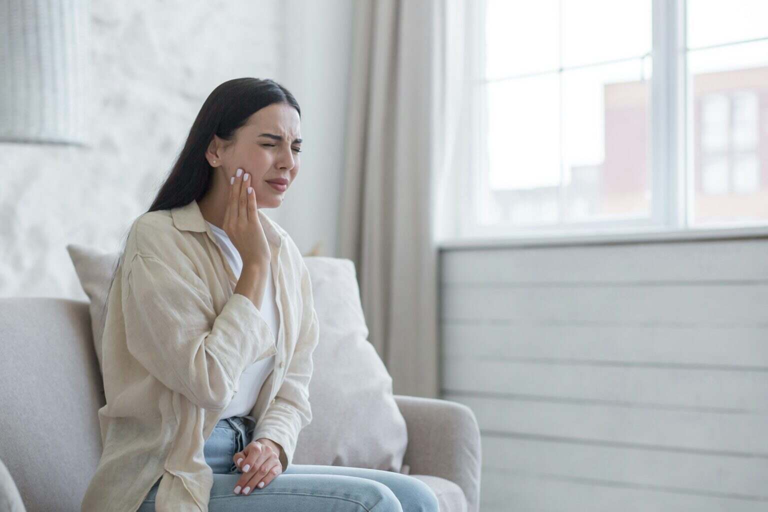 A woman is sick at home alone, has a severe toothache, a brunette is sitting on the sofa