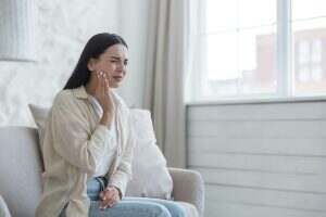 A woman is sick at home alone, has a severe toothache, a brunette is sitting on the sofa