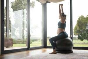 Blonde pregnant woman practicing yoga in the living room next to the windows