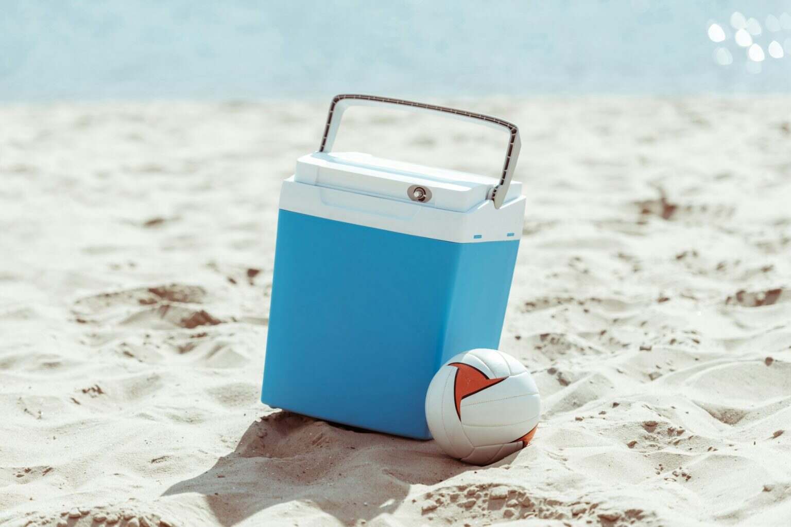 blue cooler box and volleyball ball on sandy beach