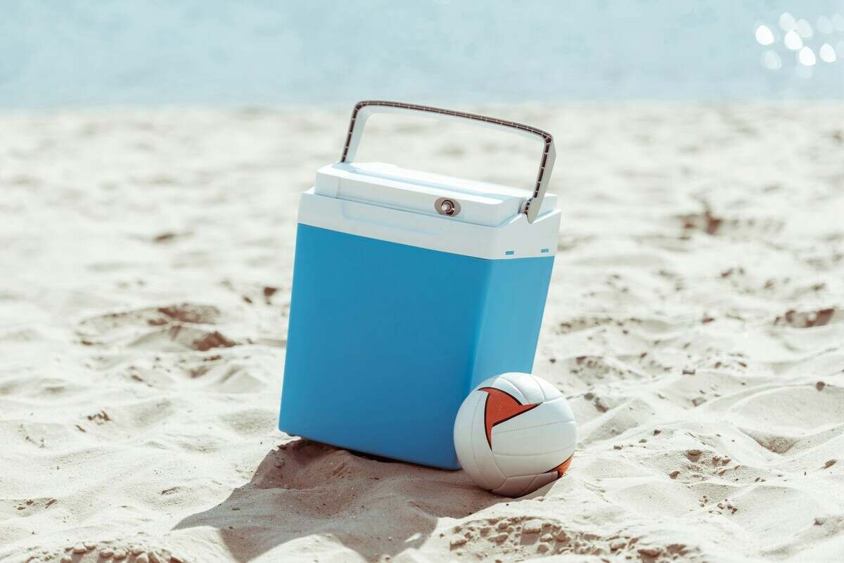 blue cooler box and volleyball ball on sandy beach