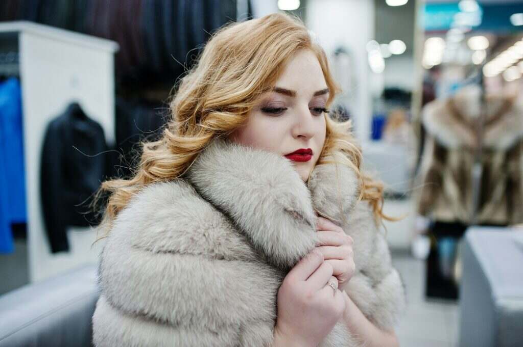 Elegance blonde girl in fur coat at the store of fur coats and leather jackets.