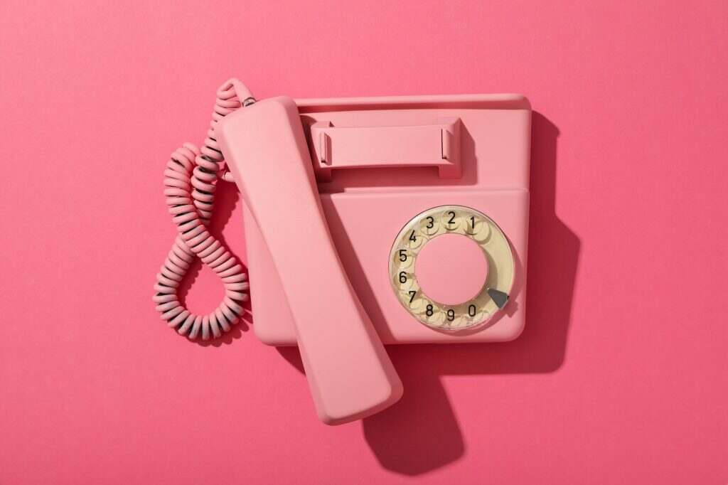 Pink landline phone on pink background, top view