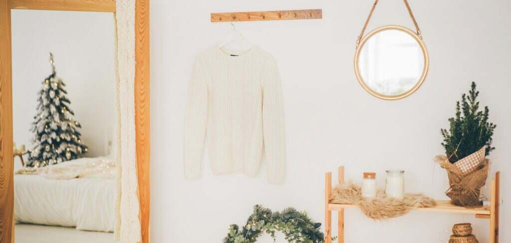 Scandinavian hallway interior with big mirror and shoe storage bench near white wall.