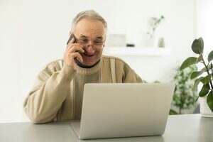 senior man looking at laptop and phone calling at home.