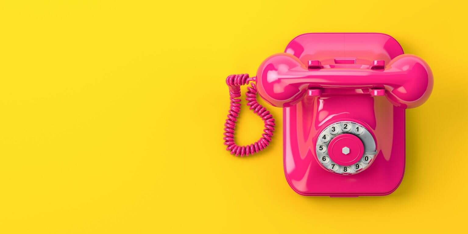 Vintage pink telephone on yellow background.