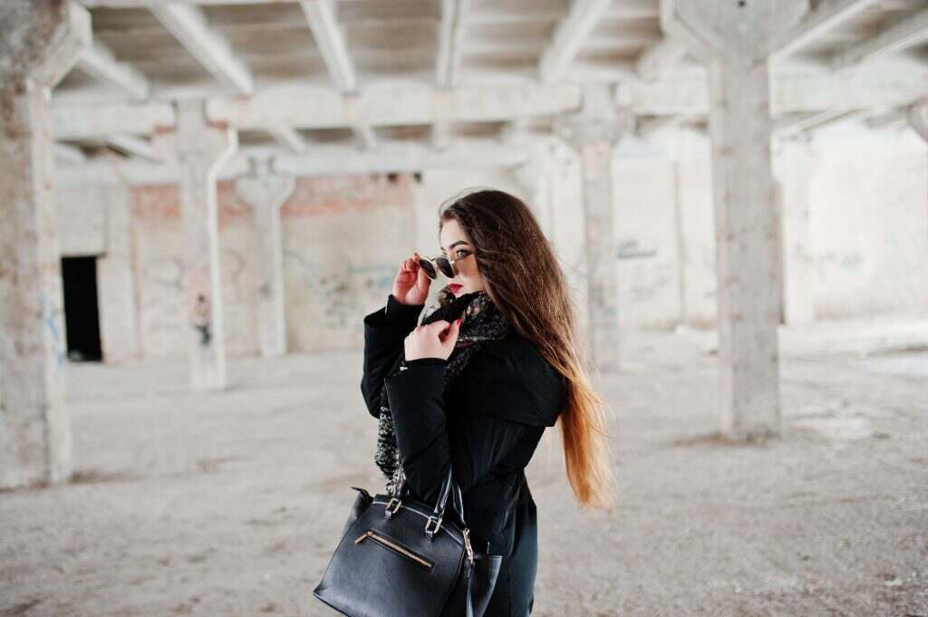Brunette stylish casual girl in scarf and handbag against abandoned factory place.
