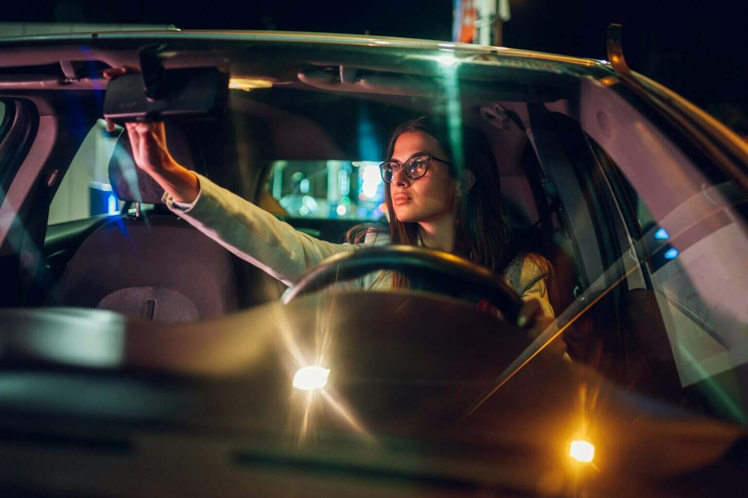 Business woman adjusting rearview window in a car at night