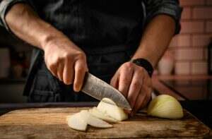 Chief hands cutting onion to slices at kitchen